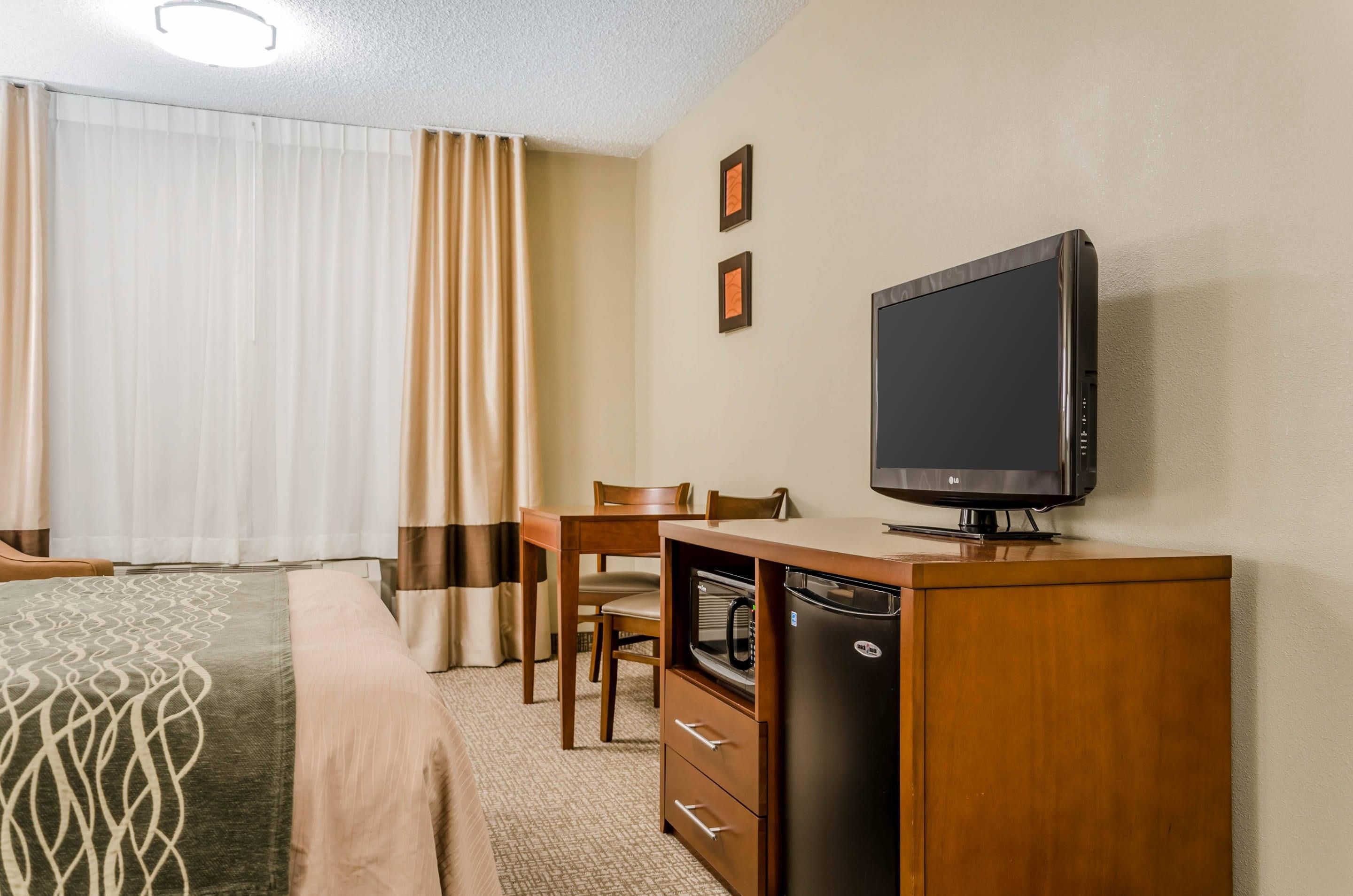 A hotel room with a bed, a desk with a television, a microwave, and a chair.