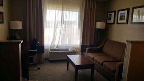 A hotel room with a sofa, a small table, a desk with a lamp, a chair, and a window with curtains. - Comfort Inn Idaho Falls I-15 (Idaho Falls)