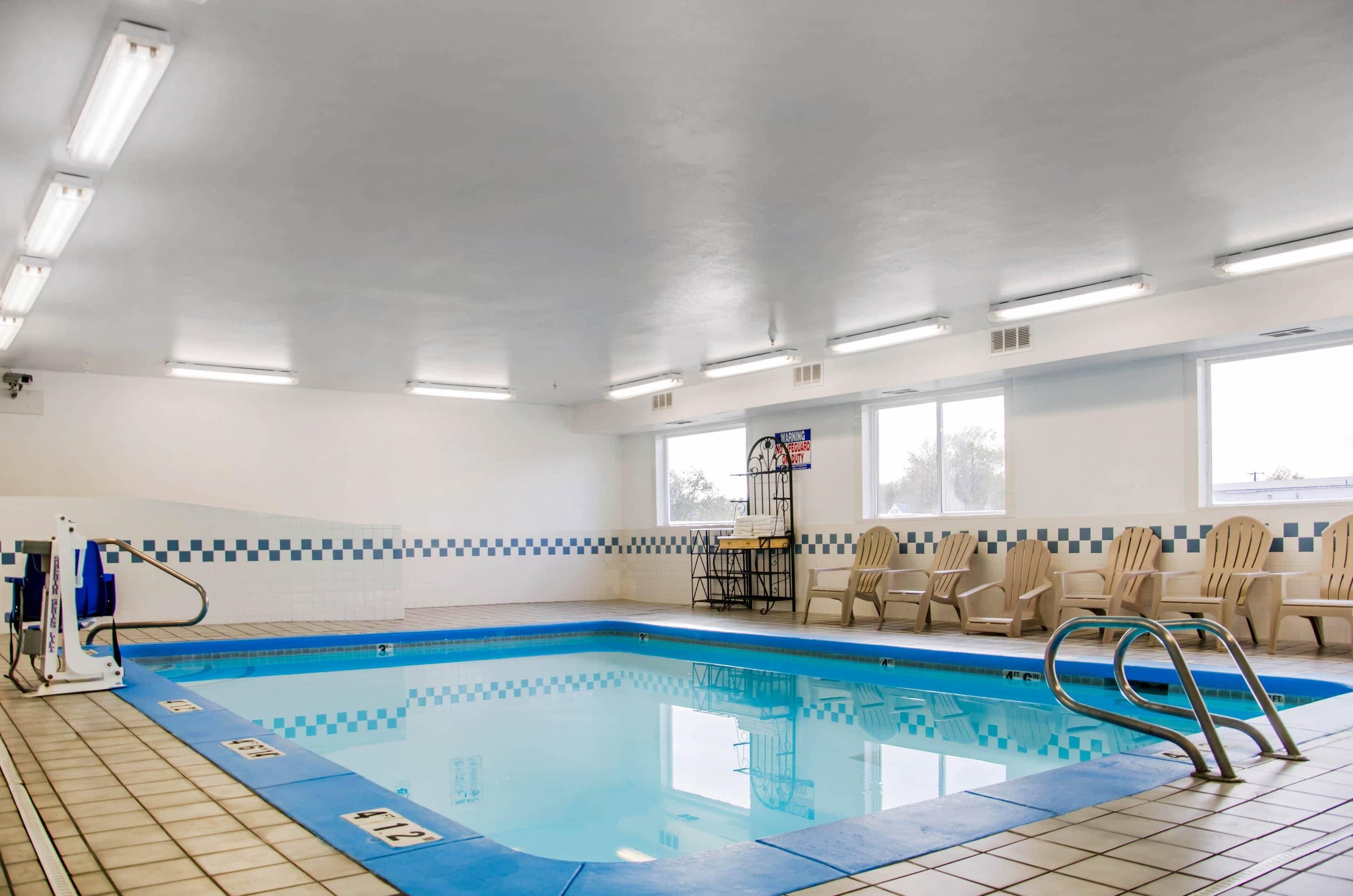 Piscina interna com piso ladrilhado, cadeira de salva-vidas e sinal de alerta na parede.