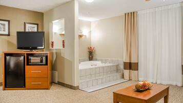 A hotel room with a television, a refrigerator, a microwave, a wooden table, and a bathroom with a bathtub and a shower curtain.