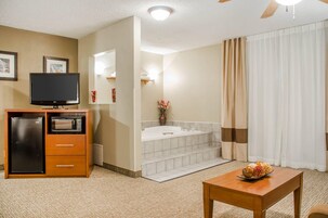 Habitación de hotel con televisión, refrigerador, microondas, una mesa de madera y un baño con bañera y cortina de ducha.