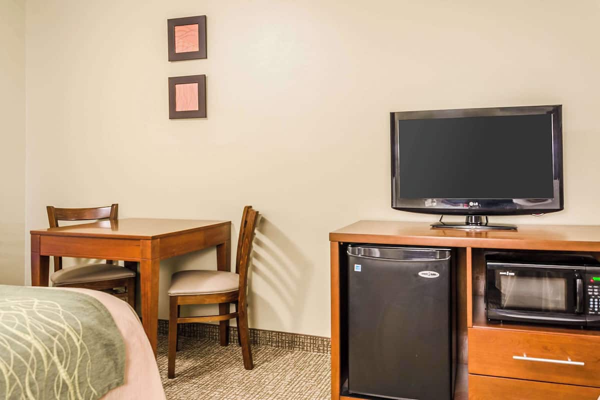 A hotel room with a bed, a wooden desk with a television, a refrigerator, and a microwave.