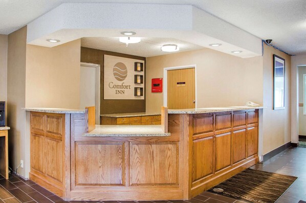 Zona de recepción de hotel con un mostrador de madera, un letrero que dice "Comfort Inn" y una puerta con la etiqueta "Vestíbulo".