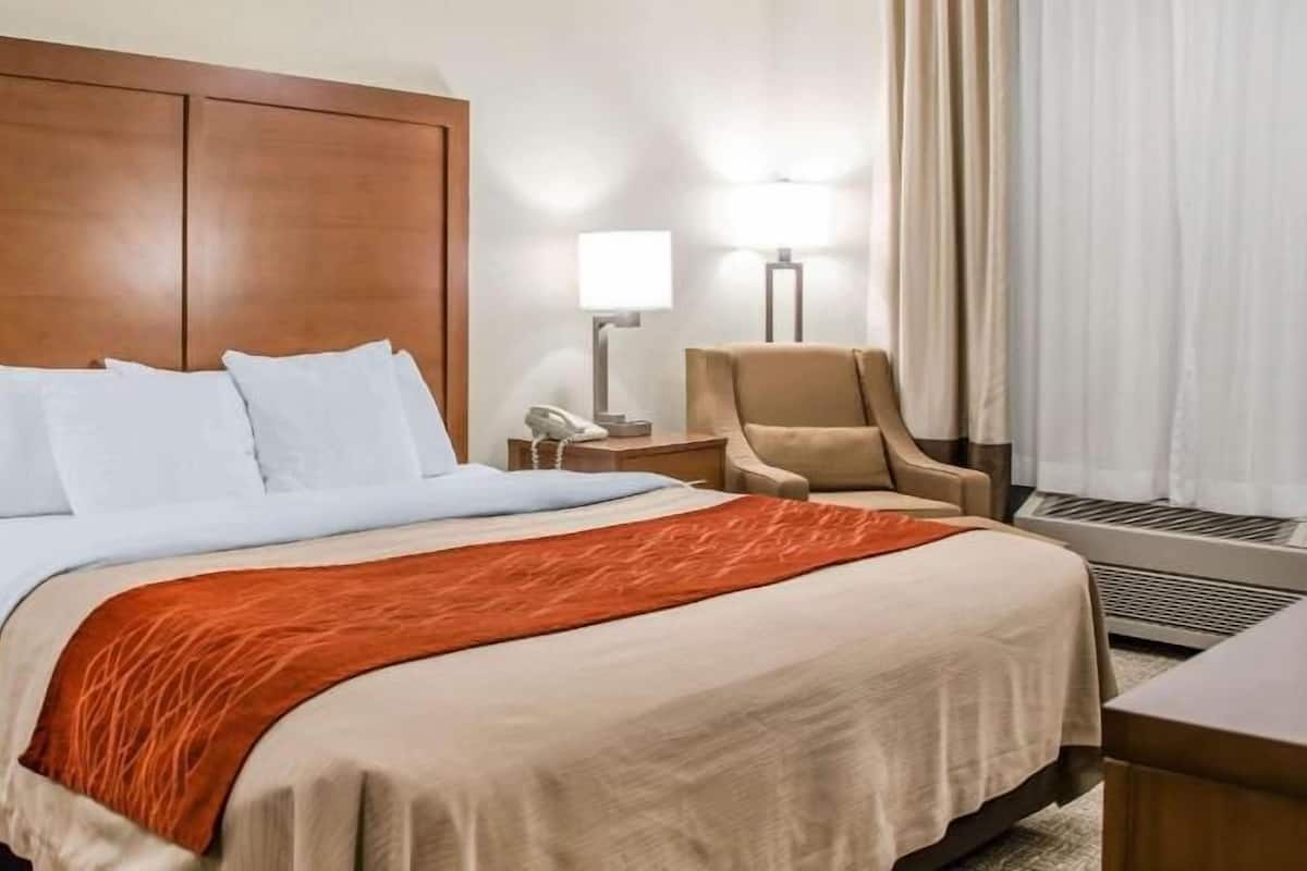 A hotel room with a large bed, a chair, a desk, a lamp, and a phone on the nightstand.