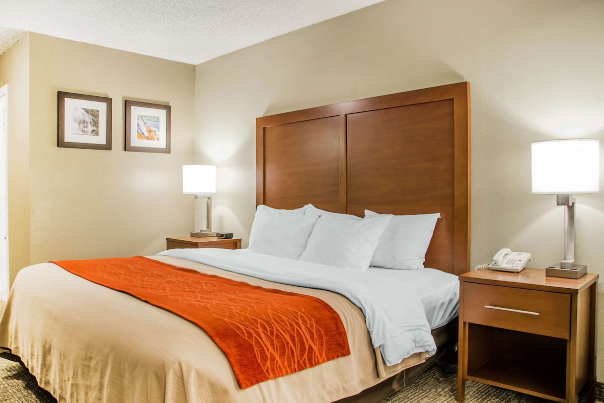 A hotel room with a large bed, two bedside tables with lamps, a wooden headboard, and two framed pictures on the wall.