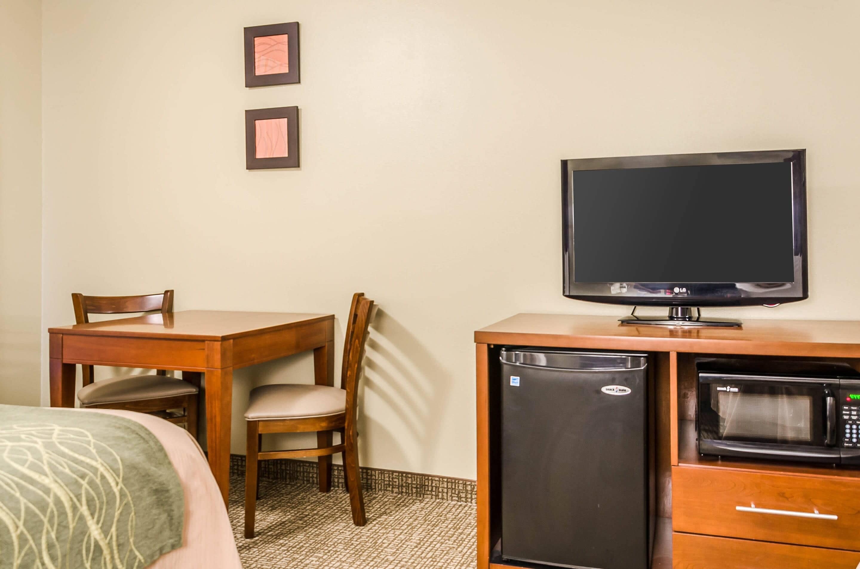 A hotel room with a wooden desk, a television, a refrigerator, and a microwave.