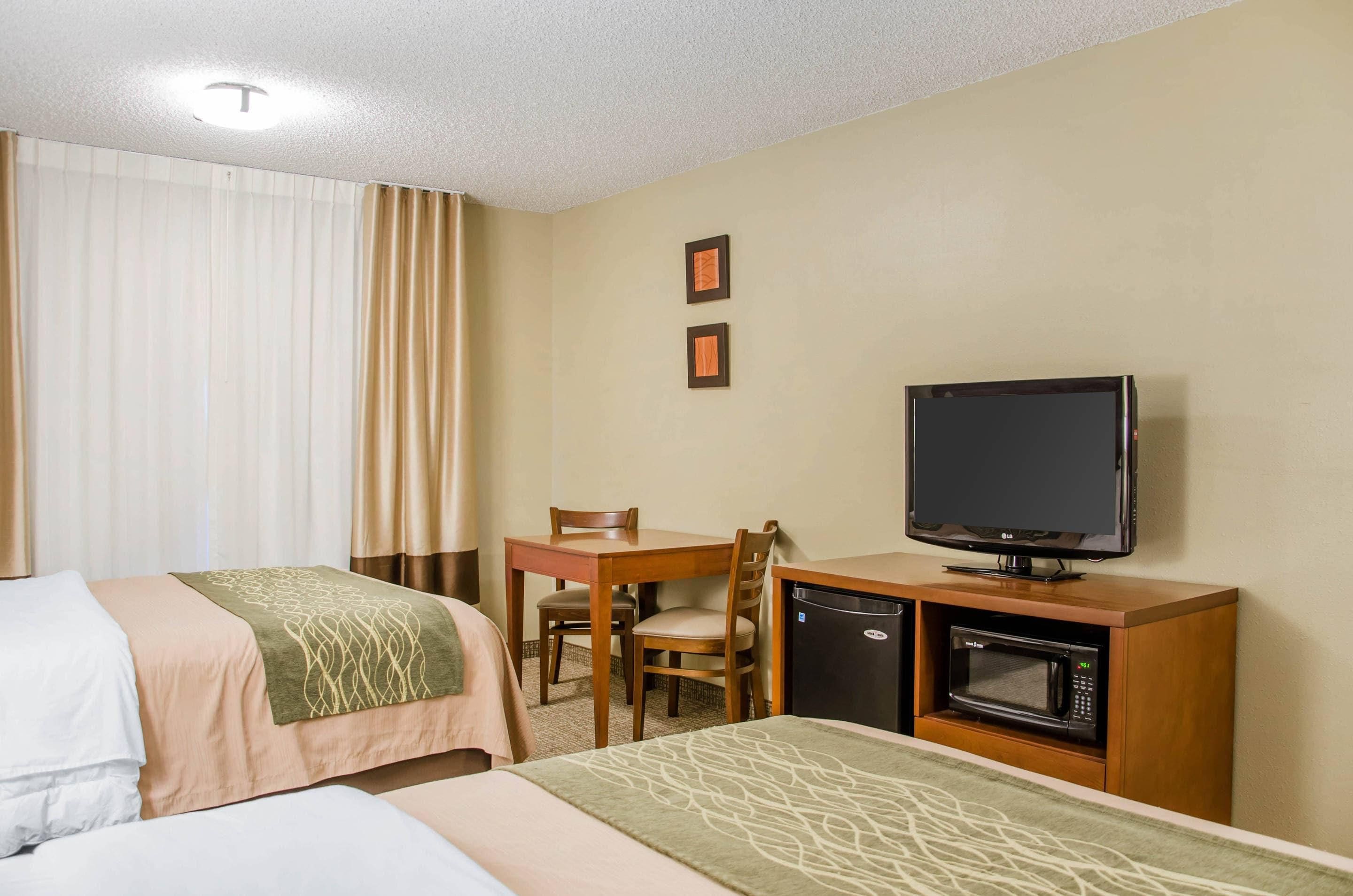 A hotel room with two beds, a desk with a chair, a television, and a microwave.