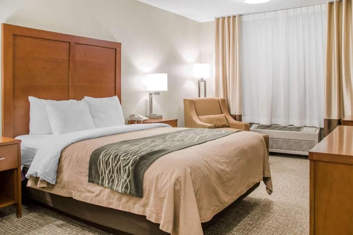 A hotel room with a bed, a chair, a desk, a lamp, and a window with curtains.