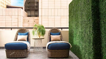 A balcony with two wicker lounge chairs, a small round table, and a potted plant.