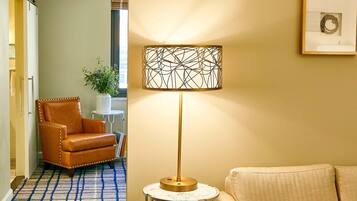 Een kamer met een kamerbreed tapijt, een leren fauteuil, een klein bijzettafeltje met een lamp en een lijst met een afbeelding aan de muur.
