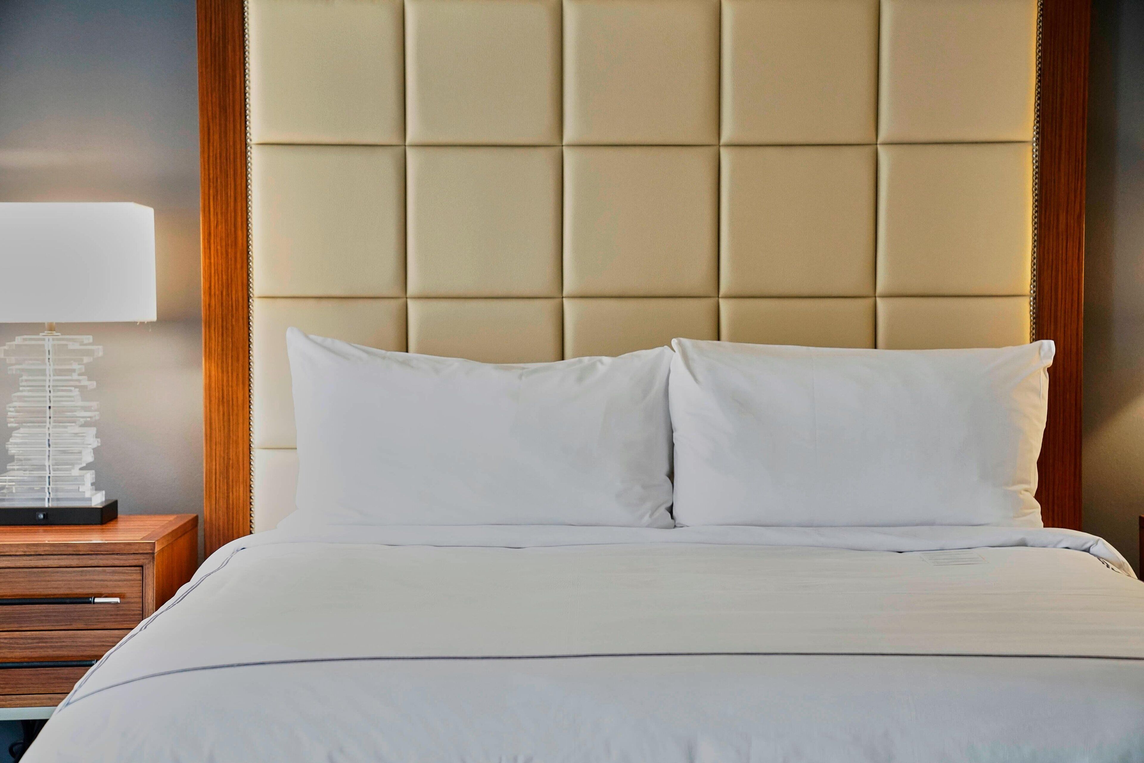 A bed with a tufted headboard, a bedside table with a lamp, and a stack of books.