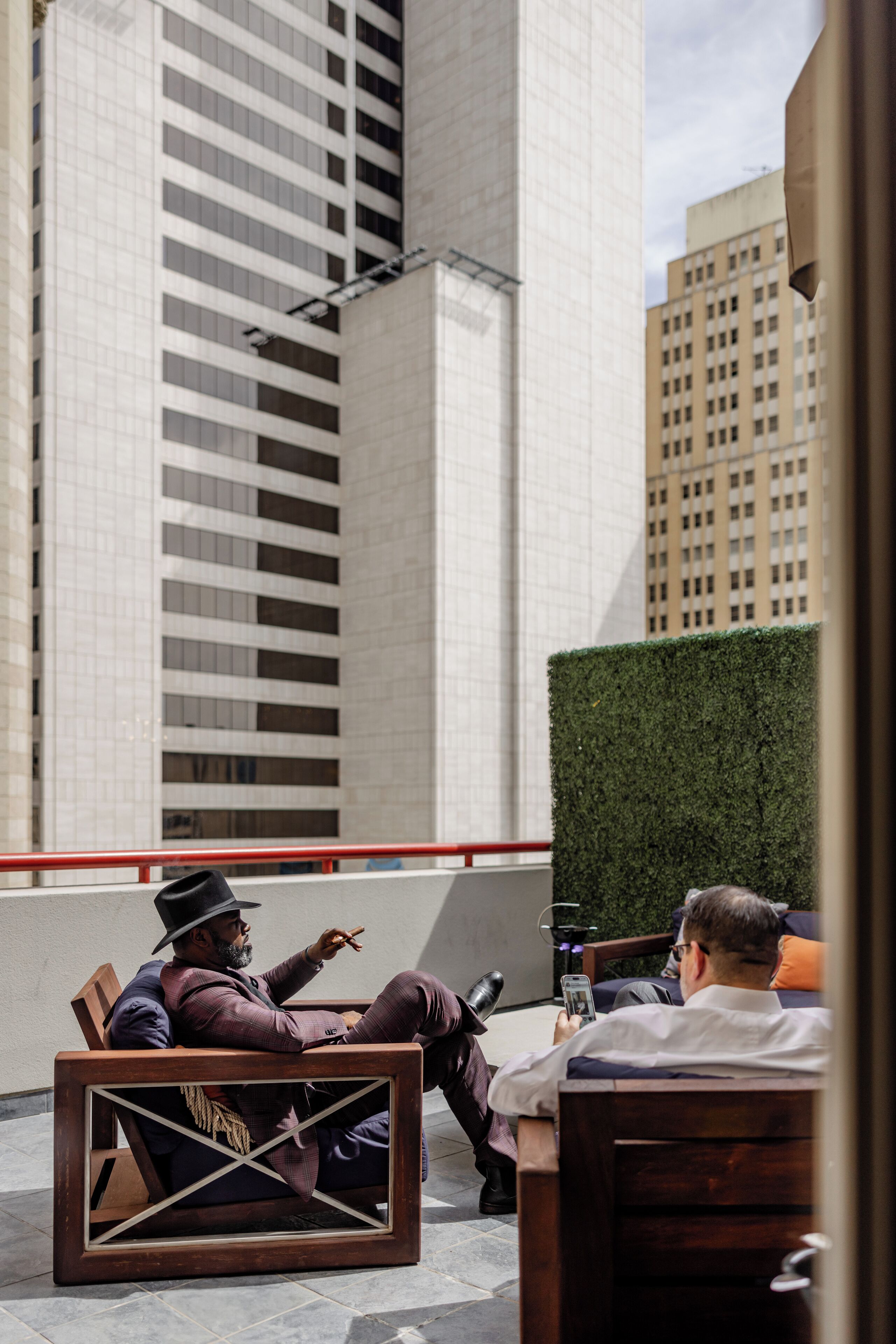 Two men sitting on outdoor furniture in an urban setting with tall buildings in the background.