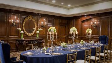 A formal dining room with a long table set for a banquet, surrounded by wooden paneling and chandeliers.