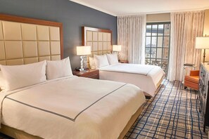 A hotel room with two beds, a large window with curtains, a patterned carpet, and a wooden headboard.