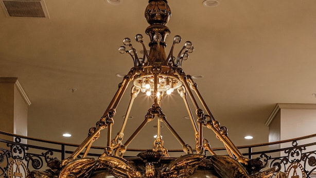 Un gran candelabro con varios niveles y luces, interior de madera y una escalera con barandilla.