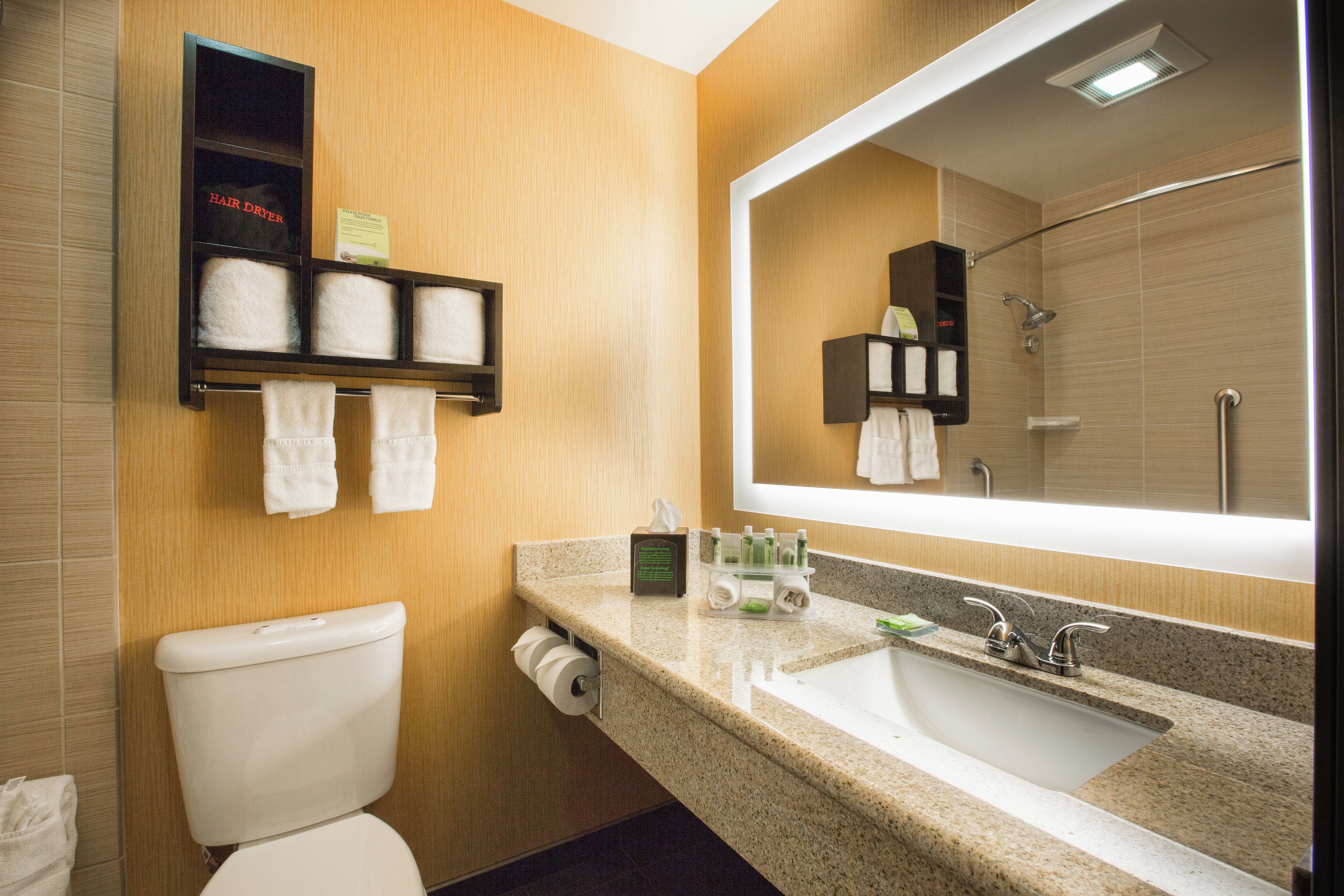 A bathroom with a toilet, sink, mirror, towel rack, and a hair dryer shelf.