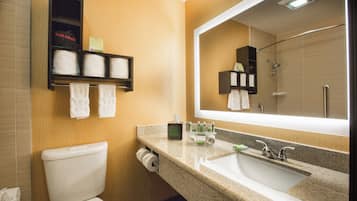 A bathroom with a toilet, sink, mirror, towel rack, and a hair dryer shelf.