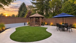 Ein Garten mit einem Pavillon, Terrassenmöbeln und einem gepflegten Rasen.