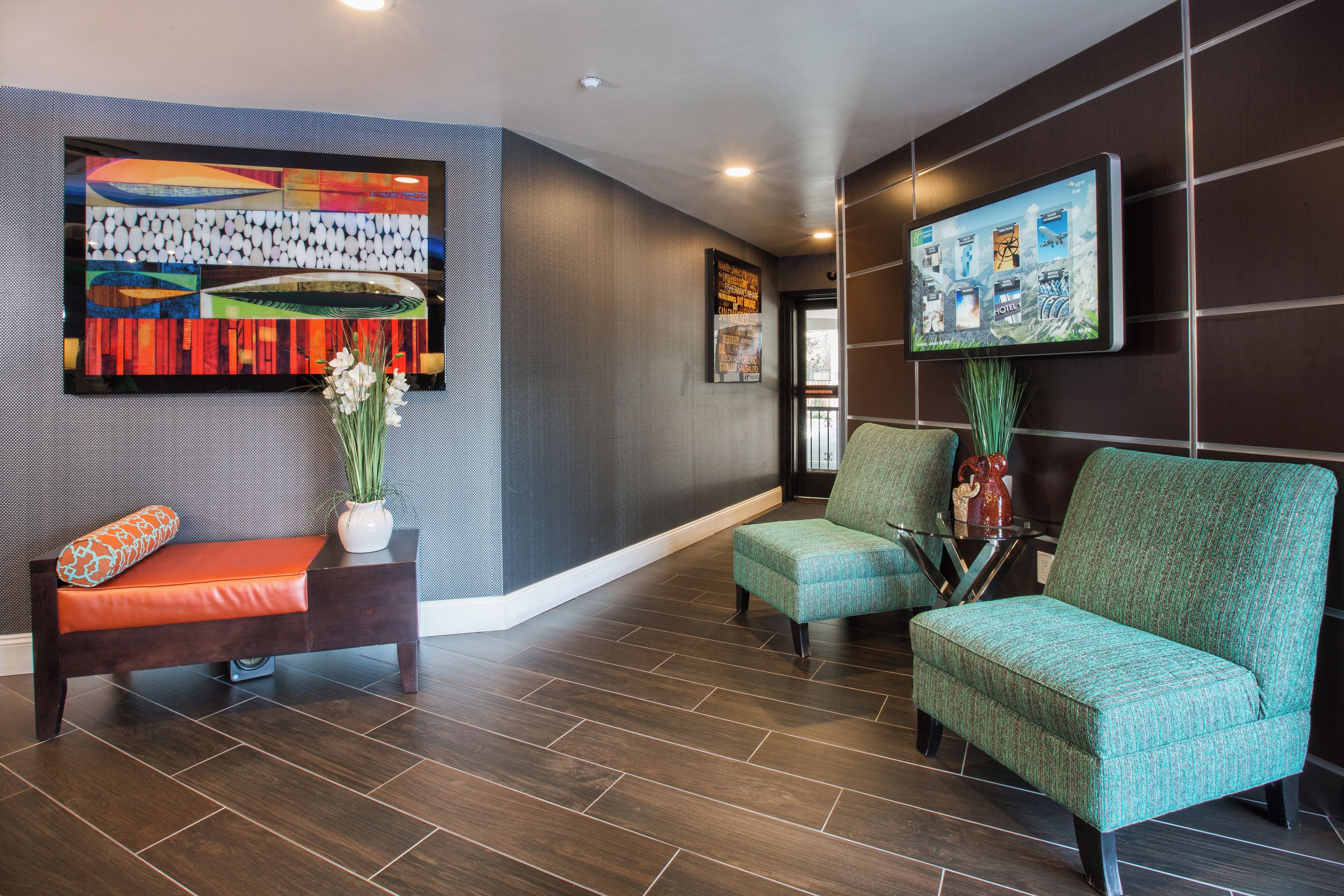 A lobby with a reception desk, two armchairs, a sofa, a wall-mounted TV, and a large abstract painting.