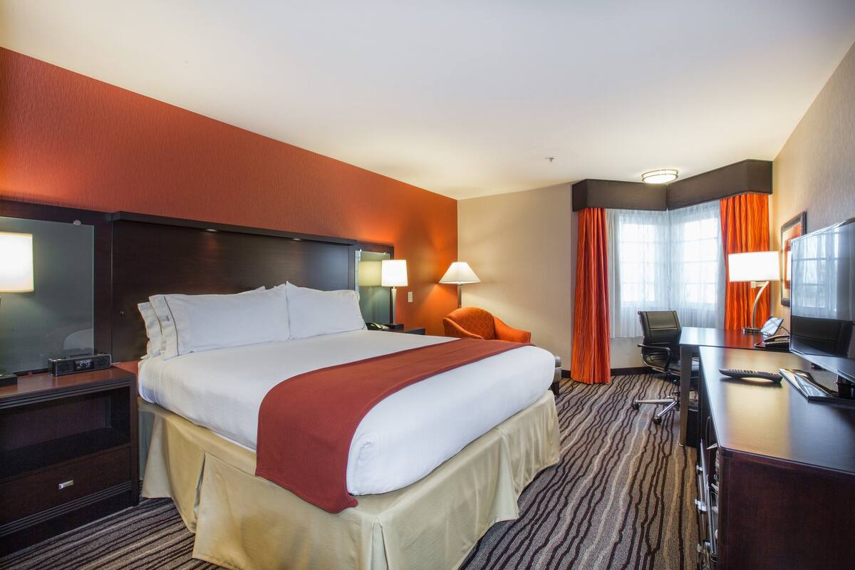 A hotel room with a large bed, a desk with a computer, a chair, and a TV.