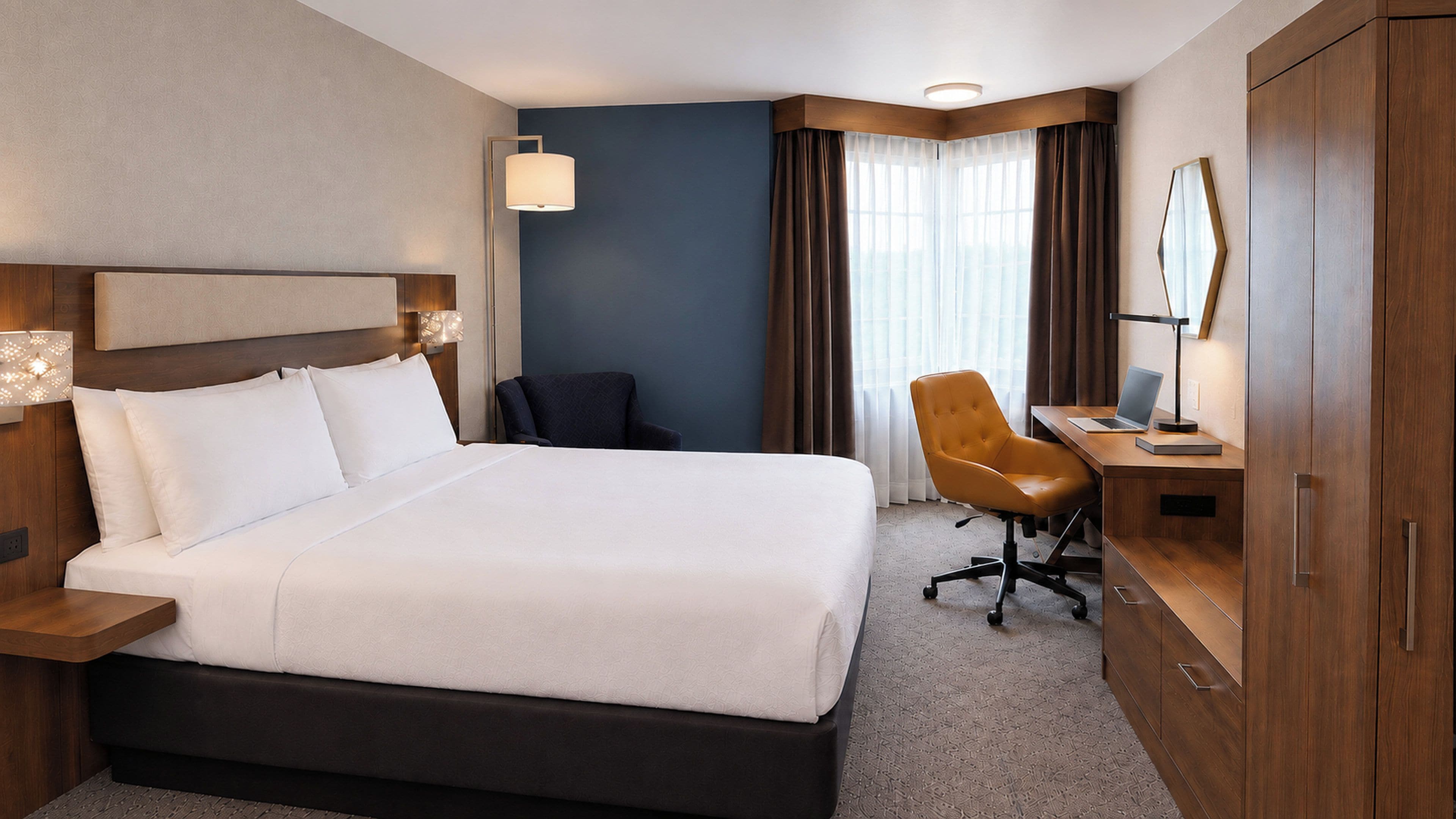 Una habitación de hotel con una cama grande, un escritorio con una computadora portátil, una silla y un armario.