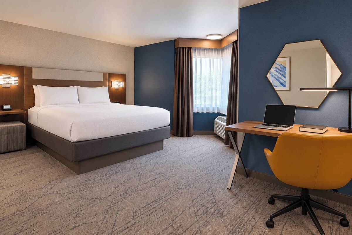 A hotel room with a bed, desk, chair, and a large mirror.