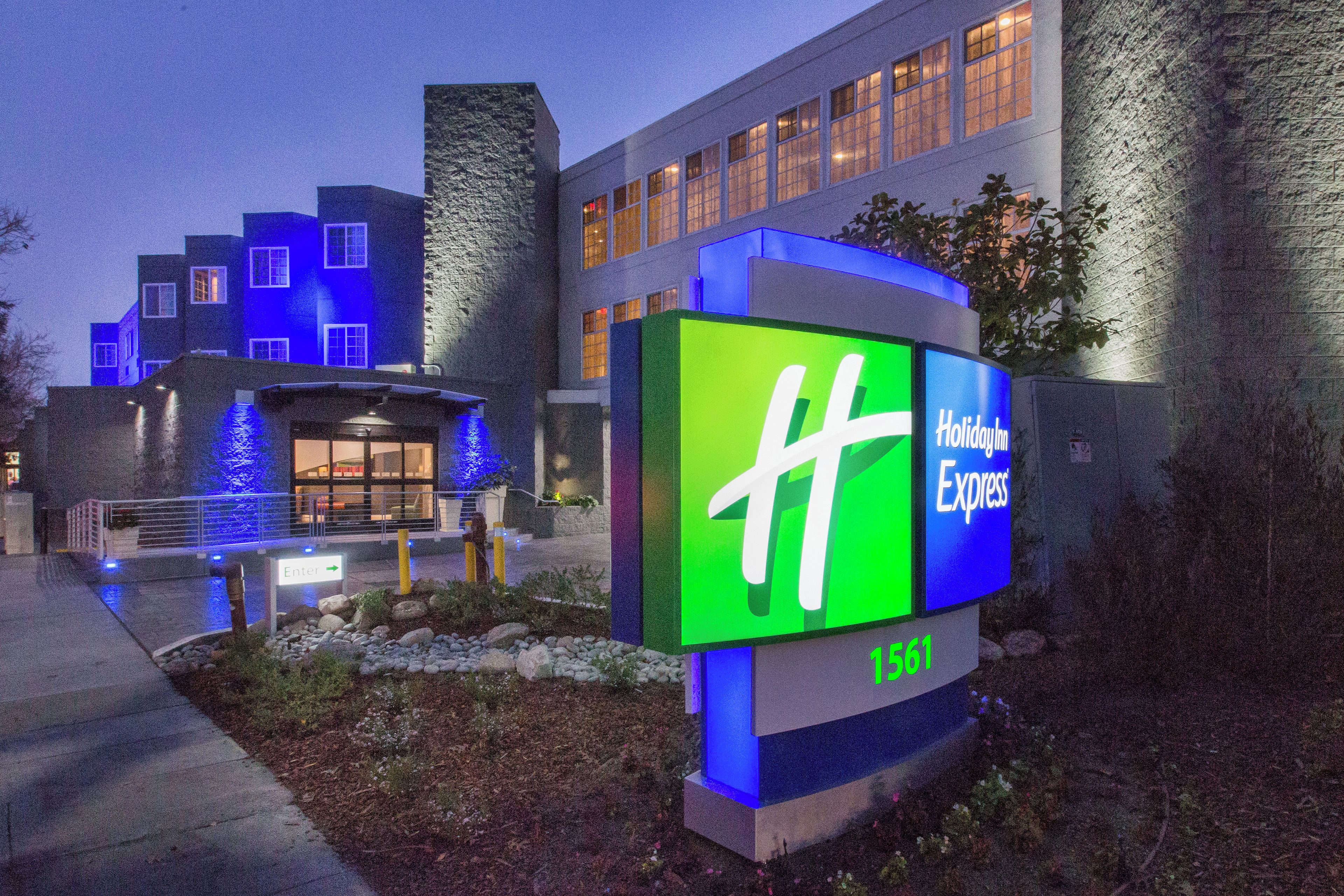 A hotel entrance with a large illuminated sign, a stone facade, and a modern building in the background.