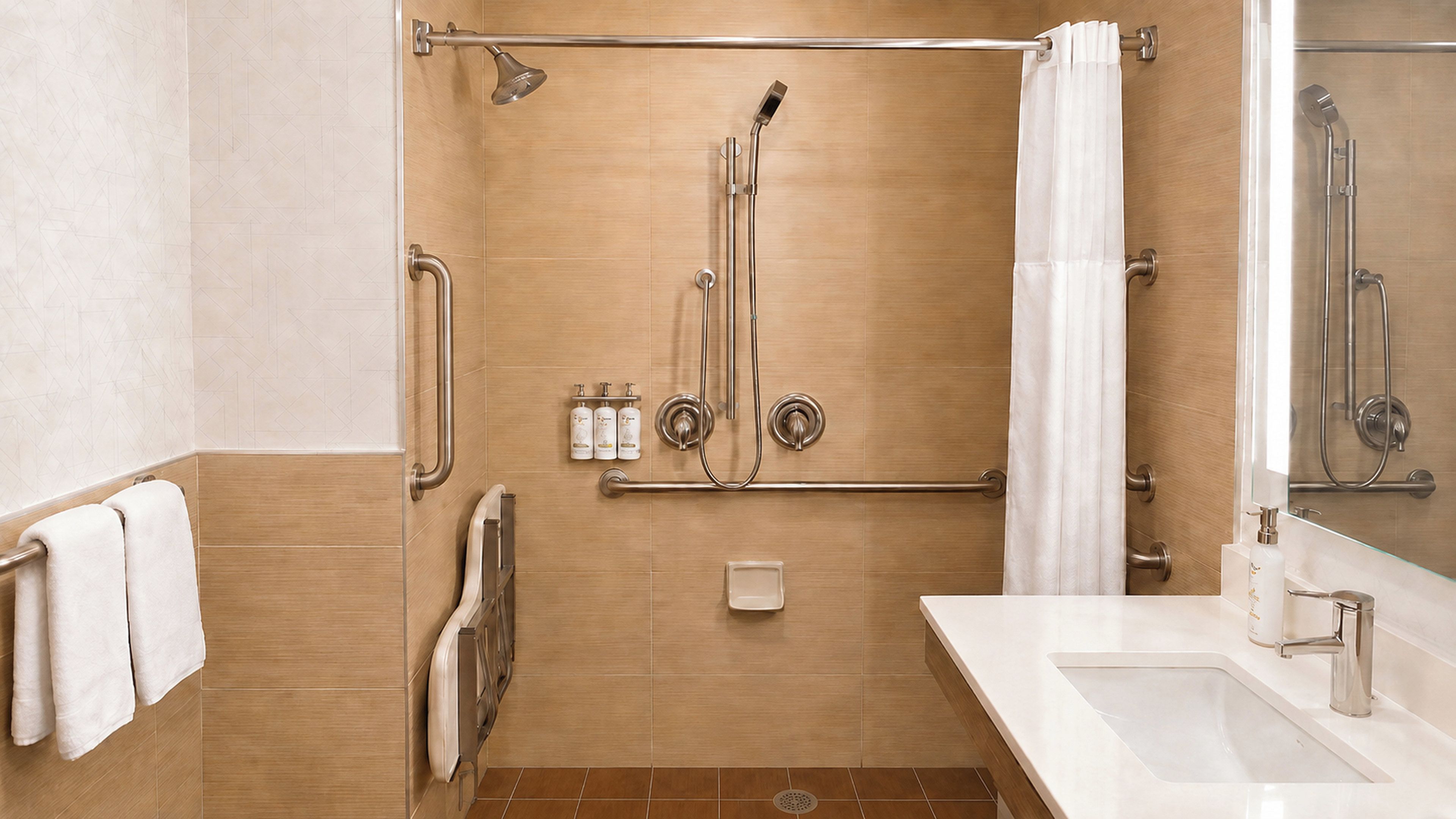 Un baño moderno con cabina de ducha a ras de suelo, barras de apoyo, mampara de vidrio y tocador con lavabo.