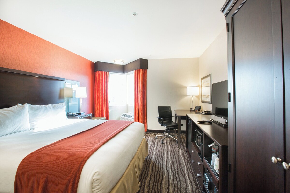 Una habitación de hotel con cama, escritorio, silla, televisor y armario.