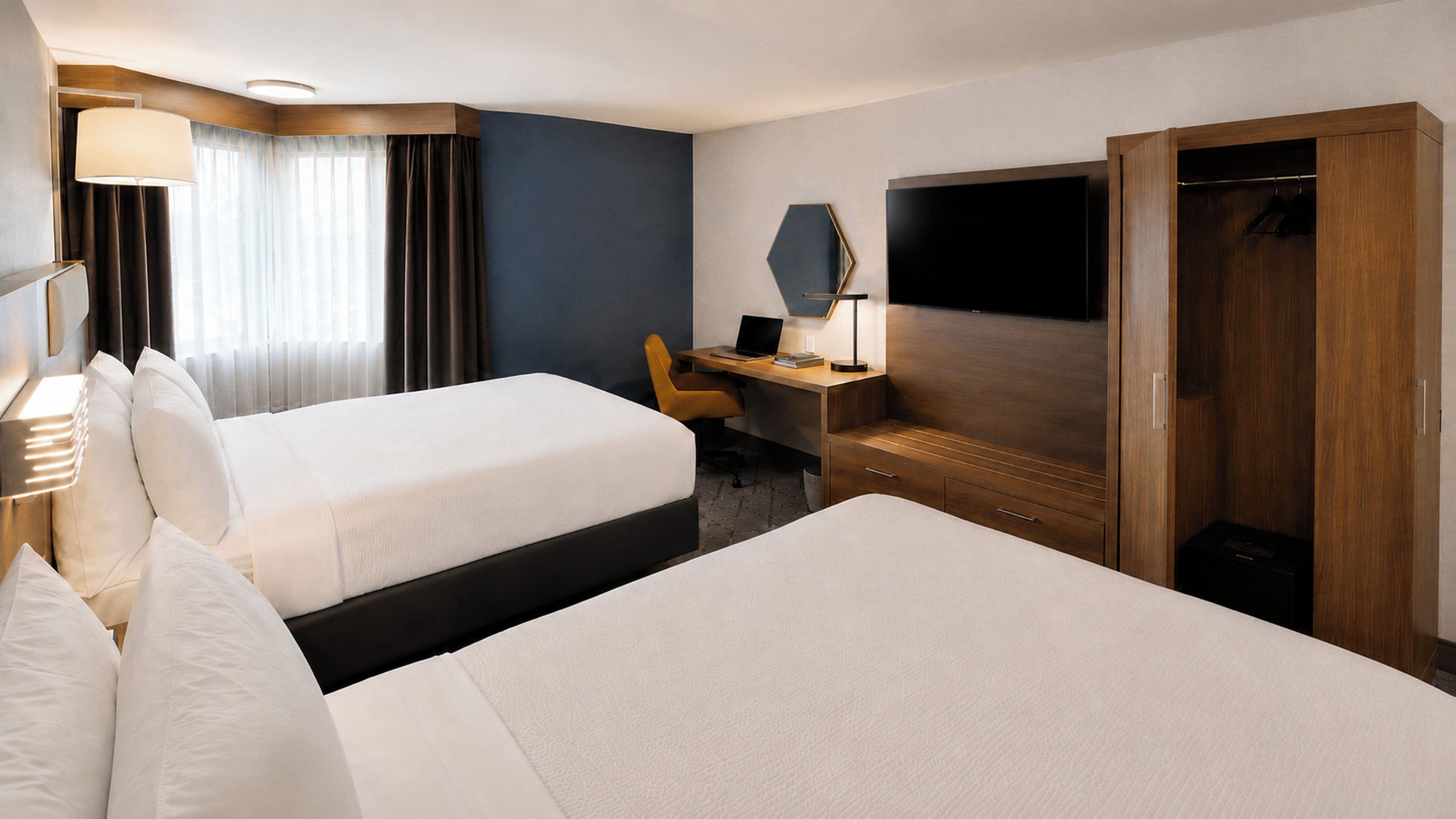 Habitación de hotel con dos camas, un escritorio, una silla, un televisor y un armario.