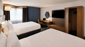 Quarto de hotel com duas camas, uma escrivaninha, uma cadeira, televisão e guarda-roupa.