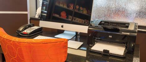 Un comptoir d’accueil d’hôtel équipé d’un ordinateur de bureau, d’un téléphone et d’une imprimante.