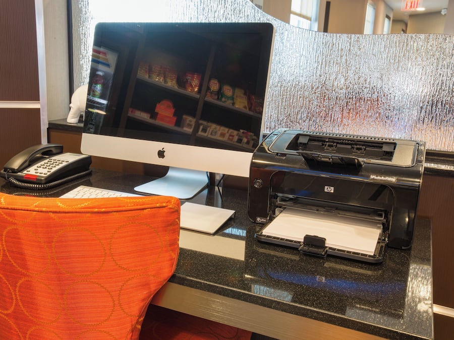 A hotel reception desk with a desktop computer, a telephone, and a printer.