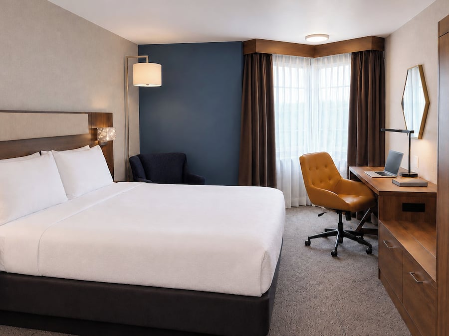 A hotel room with a large bed, a desk with a laptop, a chair, and a wardrobe.