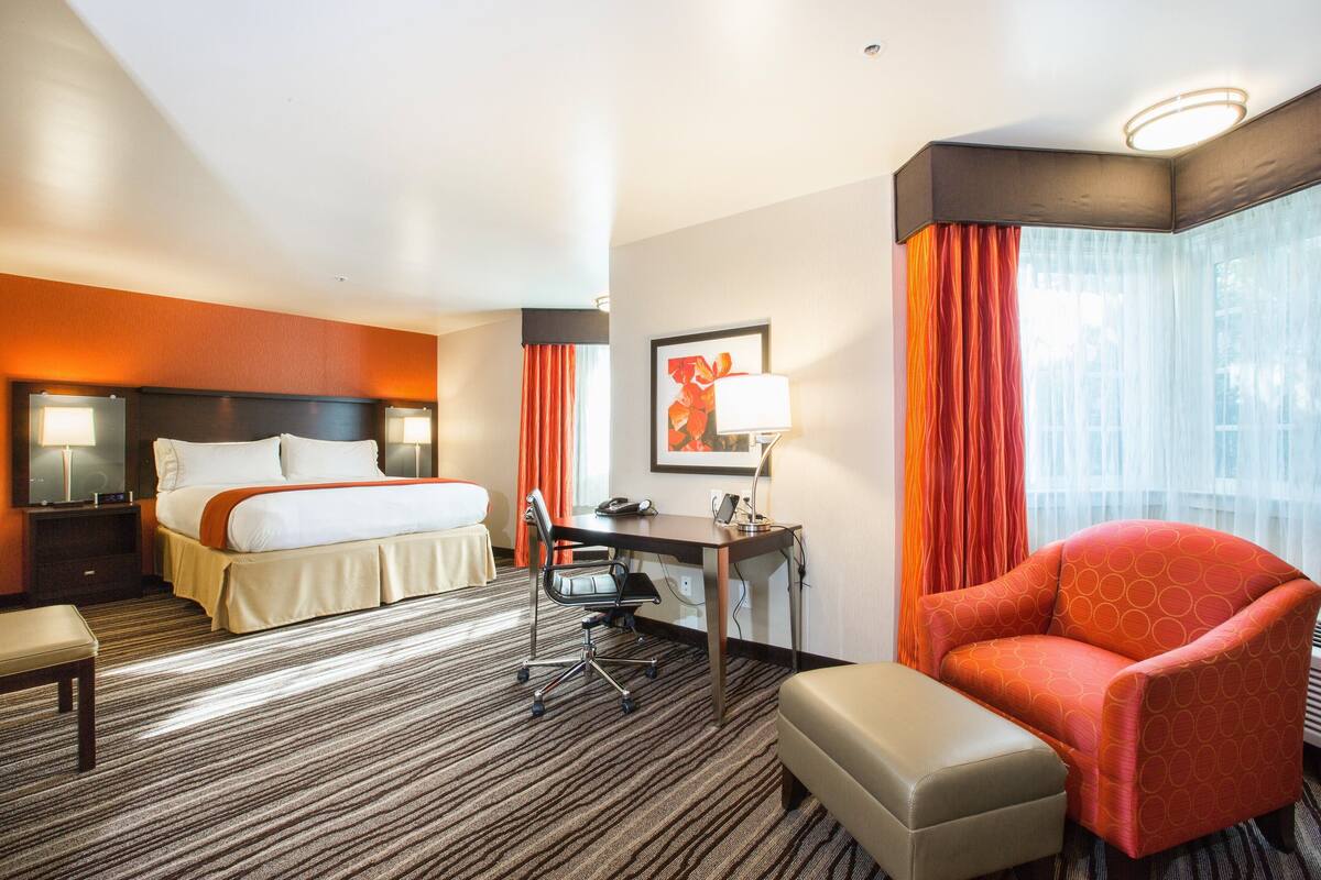 A hotel room with a bed, desk, chair, and a small table.
