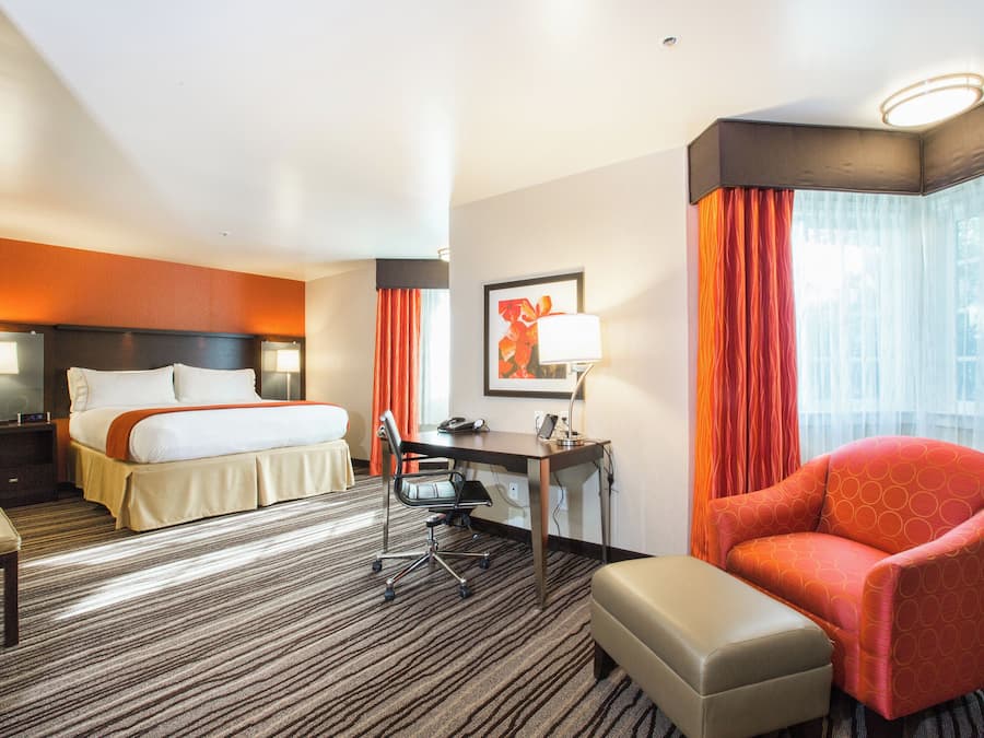 Quarto de hotel com cama, escrivaninha, cadeira e uma mesinha.