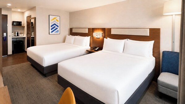 A hotel room with two beds, a desk, a chair, a microwave, and a coffee machine.