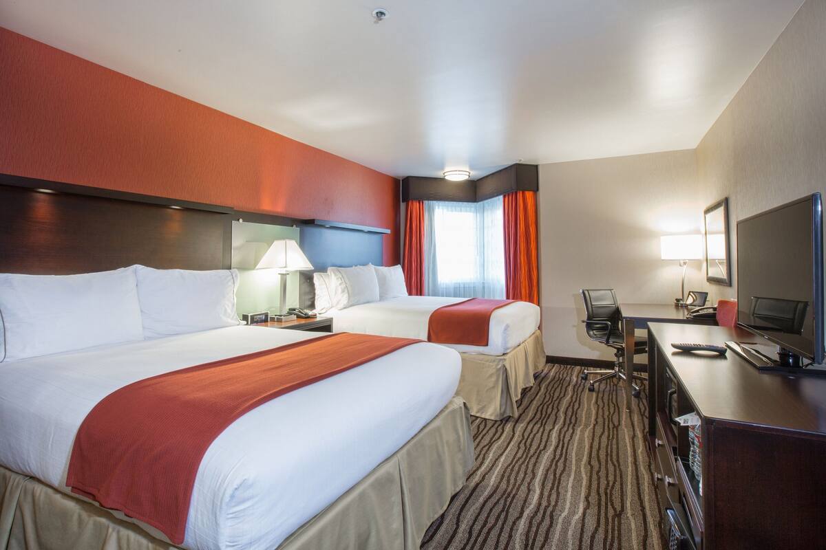 A hotel room with two beds, a desk with a computer, a TV, and a window with curtains.
