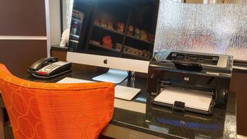 A hotel reception desk with a desktop computer, a telephone, and a printer.