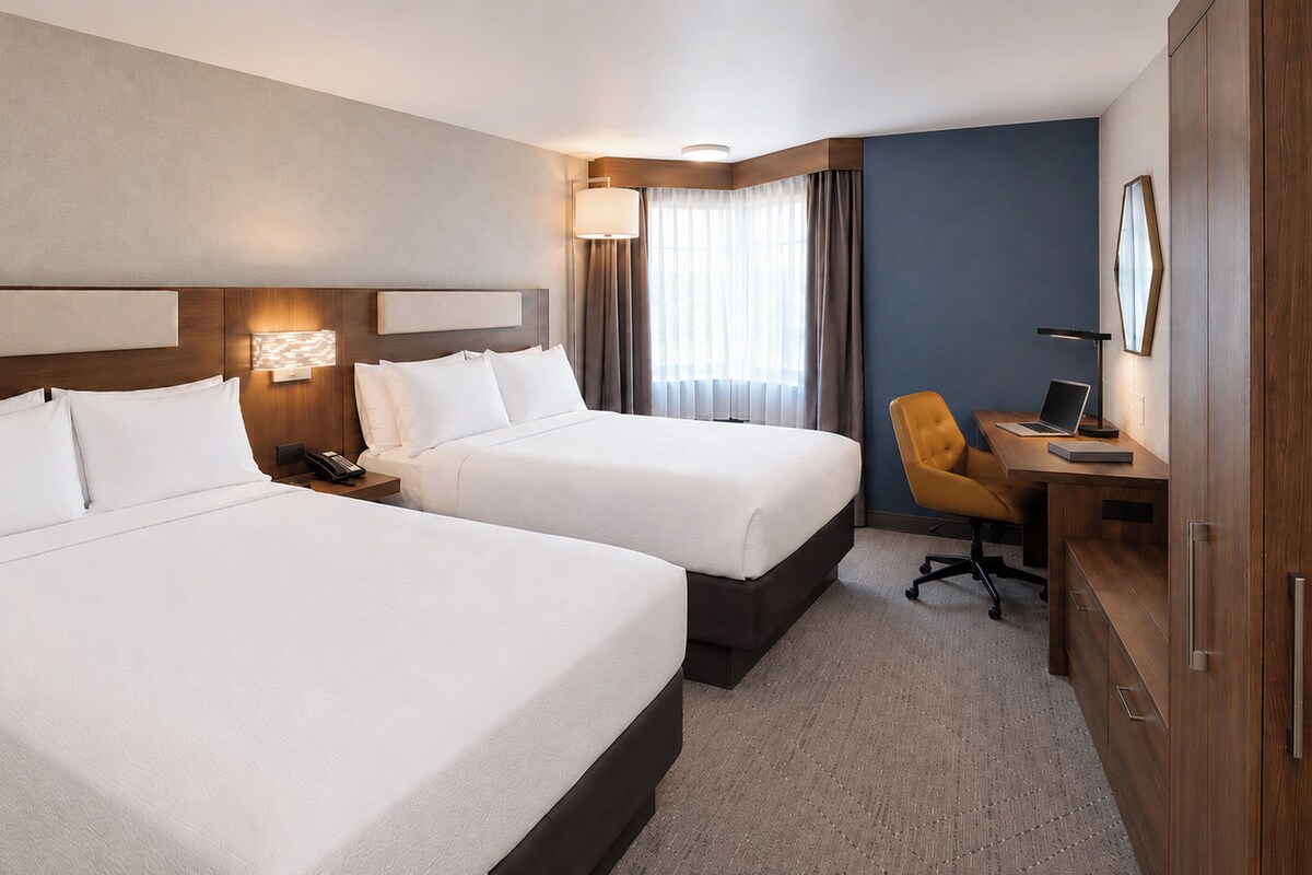 A hotel room with two beds, a desk with a chair, a lamp, and a wardrobe.
