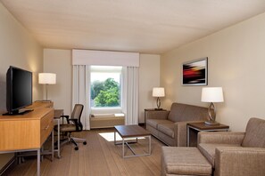 Habitación de hotel con televisión, escritorio, silla de oficina, sofá y dos mesitas de noche con lámparas.