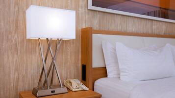 Una cama bien hecha con ropa de cama blanca, una mesita de noche con una lámpara, un teléfono y un cuadro en la pared.
