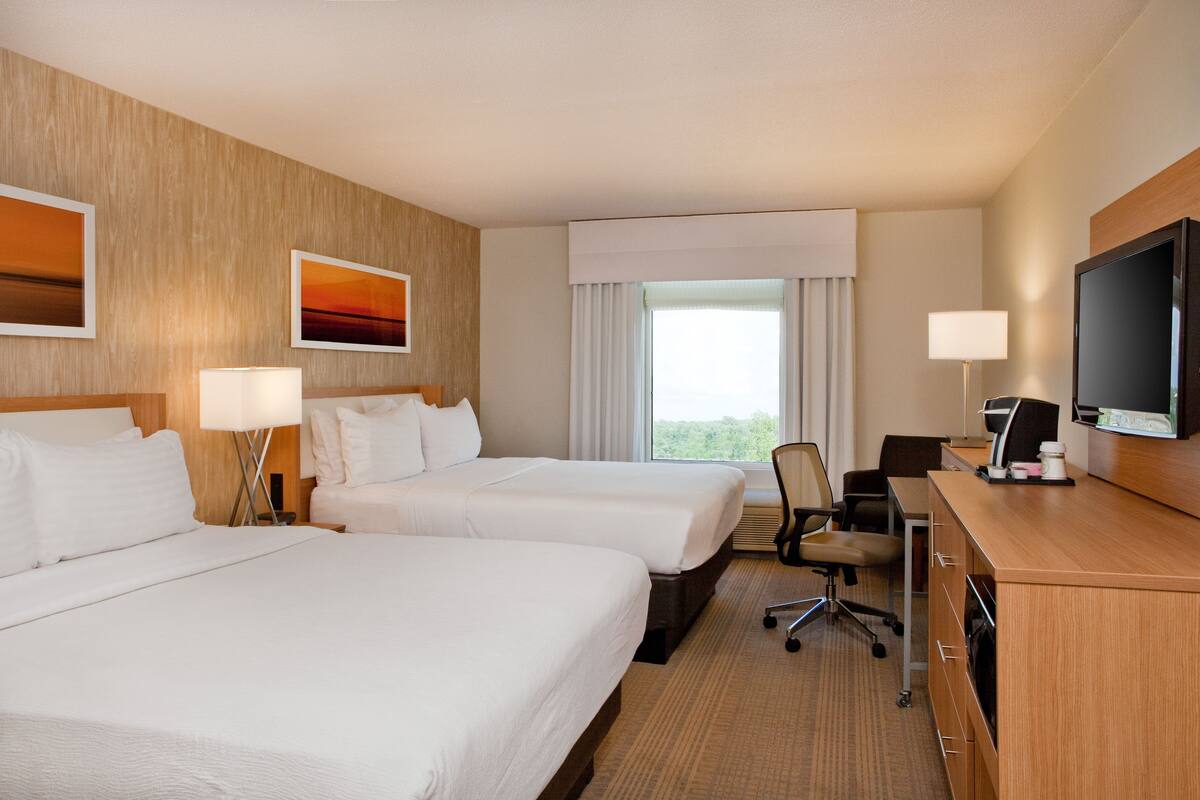 A hotel room with two beds, a desk with a computer, a TV, and a window with curtains.