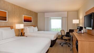 A hotel room with two beds, a desk with a computer, a TV, and a window with curtains.