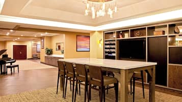 Un hall d’hôtel spacieux avec un piano, un comptoir d’accueil, une grande table à manger entourée de chaises et un téléviseur.