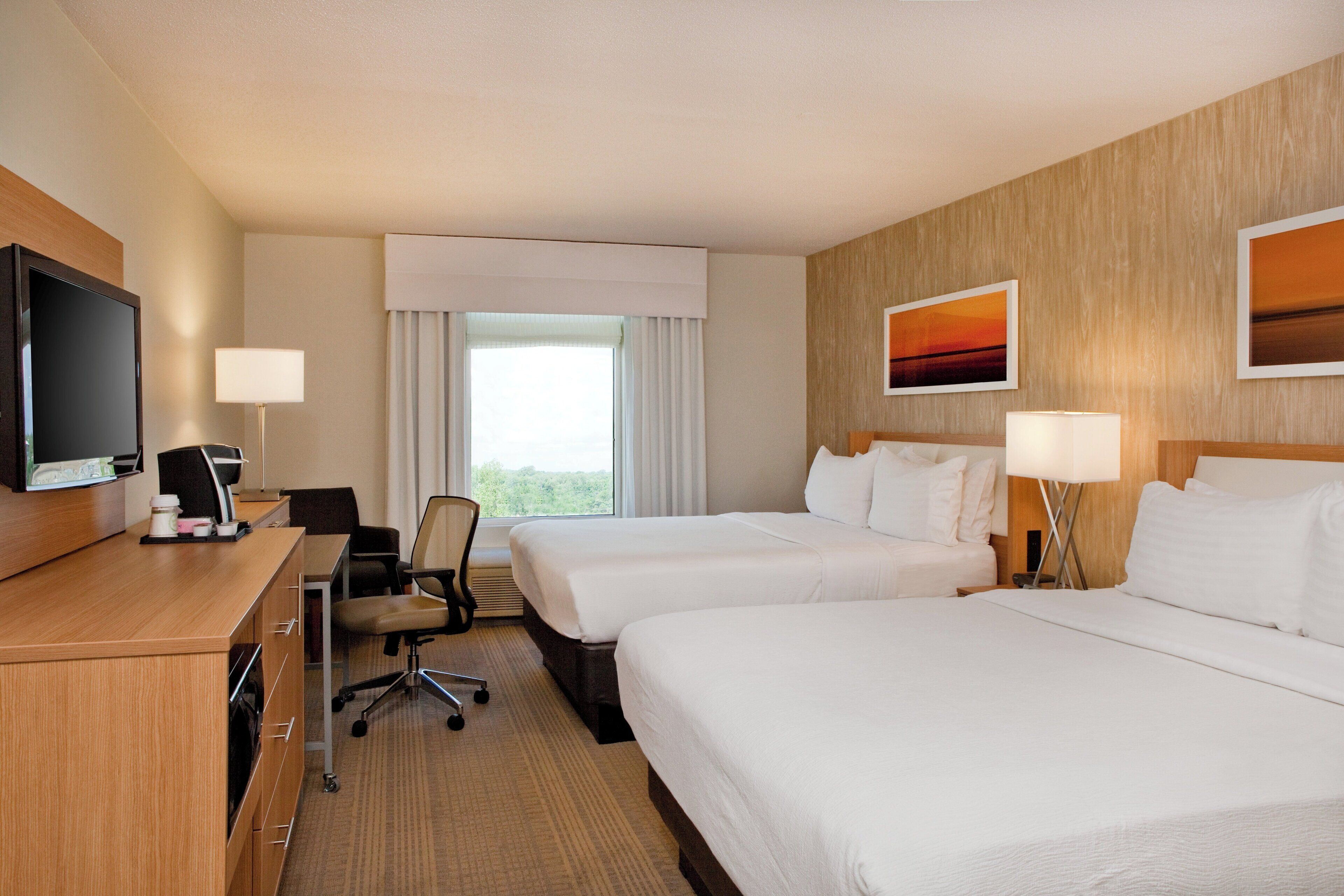 A hotel room with two beds, a desk with a television, a chair, and a window with curtains.