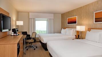 A hotel room with two beds, a desk with a television, a chair, and a window with curtains.