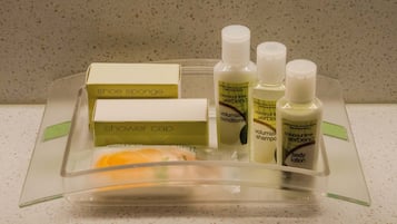 Una bandeja de plástico transparente con varios artículos de aseo, como un gorro de ducha, loción corporal y champú.