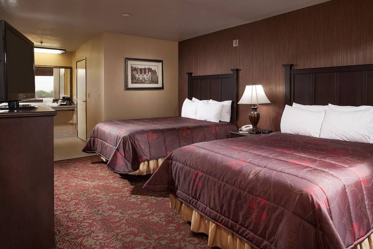Ein Hotelzimmer mit zwei Betten, einem Schreibtisch, einer Lampe und einem gerahmten Bild an der Wand.