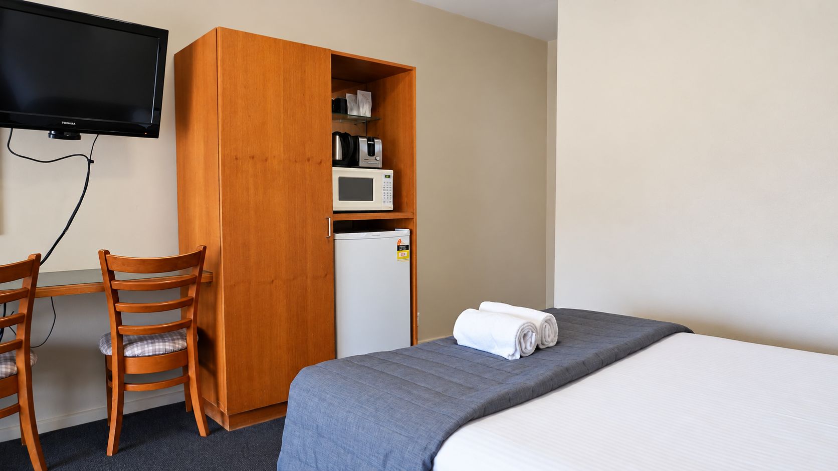 Ein Hotelzimmer mit Bett, Schreibtisch mit Stuhl, Wandfernseher, Mikrowelle und Kühlschrank.